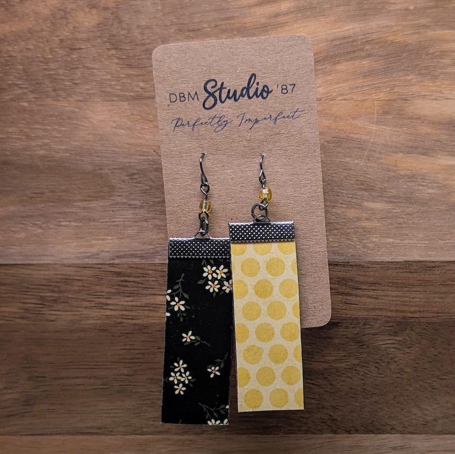 Medium rectangle scrapbook paper earrings with a felt core. Black with yellow flower front and yellow with golden yellow circle back. Pewter colored finishes and a yellow bead. Front and back are shown